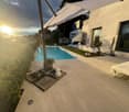 Swimming pool, tiled patio, umbrella, lounger, plants, view of the sunset