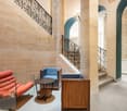 Ornate stone walls, wrought iron railings, arched doorways, wooden furniture, and a modern seating area with red and blue chairs.