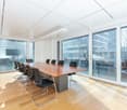 Meeting room with long wooden table, black chairs, wooden floors, large windows, white walls, glass doors