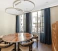 circular wooden table, 6 chairs, arched windows, dark curtains, warm lighting