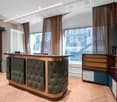 a large window allows an external view, a television on the wall, a wooden wardrobe, a reception desk, a trash can