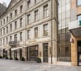 Urban building facade, multiple shops, glass doors, white awnings, potted plants, signage