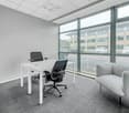 A desk with two chairs, a couch, carpeted floor, and large windows overlooking a parking lot