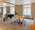 modern interior, beige walls, beige carpet, round wooden table with office chair, bookshelf, potted plants, large windows