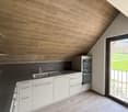 Attic kitchen with wooden ceiling, white cabinets, built-in oven and sink, hardwood flooring, and access to a balcony or terrace.