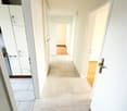 Empty hallway with tiled floor, white walls, and doors leading to different rooms.