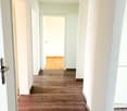 Empty hallway with wooden floors and white walls, doors on both sides