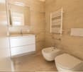 Spacious bathroom with beige marble-like tiles, a vanity unit with a sink, a toilet, and a towel warmer.