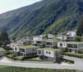 A group of modern houses, all have green roofs, surrounded by well-manicured lawns and various trees, the houses are nestled against a beautiful mountain backdrop.