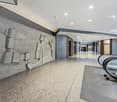 Concrete wall with abstract design, polished concrete floor, escalator, gray carpet, white ceiling with recessed lighting