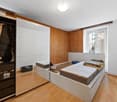 Bedroom with wooden floor, white walls, wooden paneling, large mirror, double bed, wardrobe with drawers, window with balcony access