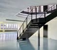 Empty room with a staircase, white walls, gray floor, large windows, metal railings