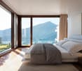 Bedroom with large windows and view of mountains and water, white walls, bed, carpet, nightstand