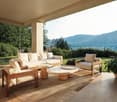covered outdoor lounge, wooden furniture, coffee tables, natural light, greenery, mountains in background