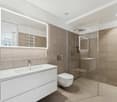 modern bathroom with white fixtures, glass shower enclosure, walk-in shower, illuminated mirror, beige tiles