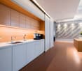 modern kitchen with wooden cabinets, white countertops, stainless steel sink, faucet, coffee machine, and a vase with flowers