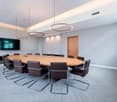 modern conference room with large oval wooden table, brown leather chairs, gray carpet, white walls, wooden door, flat screen TV