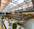 Multi-level indoor dining area with glass railings, tables, chairs, and plants