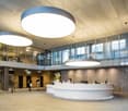 Modern office reception area, large circular lighting fixtures, glass walls, wooden paneling, front desk, large room
