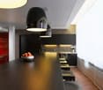 modern kitchen with large island, black cabinets, red accent wall, large pendant lights, stainless steel appliances, white flowers in vase