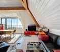 A living room with a couch, a table, a television, a rug, and a view of the ocean.