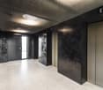 An empty hallway with shiny, patterned walls and shiny floors, four elevator doors labeled E, D, C, and 22
