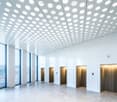 wide interior hall, white walls, gray floors, open elevator doors, windows with blinds