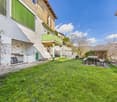 House with green balcony, green shutters, outdoor table and benches, green lawn, mountains in the background