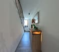 Empty hallway with white walls, wooden floor, a wooden cabinet with a lit up display, a mirror, and a switchboard.