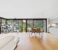 open plan living and dining area, large windows, balcony, wooden floor, dining table, modern kitchen, plants