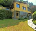 2 story house, yellow exterior, stone base, large windows, balcony, garden, pathway