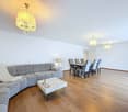 modern living room with wooden floor, gray sofa, white coffee table, dining table with chairs, chandeliers, lamps