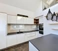 modern kitchen with white cabinets, black countertops, stainless steel sink, built-in oven and microwave, pendant lights, and a window with blinds