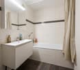 modern bathroom with a bathtub, a white vanity, a toilet, mirror, and tiled walls