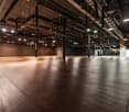 open space, wooden floors, exposed ceiling beams, suspended ceiling lights, dark walls