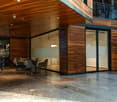 large room with modern design, wooden wall, glass doors, tables and chairs, grey floor