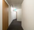 White walls, wooden door, carpeted floor, ceiling lights, wall-mounted emergency sign