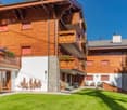 3-story wooden chalet-style apartment building with balconies, stone accents, and a grassy courtyard area