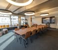 Empty meeting room with long wooden table, chairs, couch, TV, windows, ceiling lamps