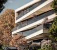 Modern white building, several balconies, glass railings, greenery around