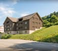 3 story house, brown exterior, multiple windows, balconies, located on a hill
