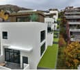Modern terraced house, white exterior, large windows, solar panels on roof, raised ground floor, scenic mountain view