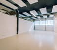 open space, white walls, white floor, suspended ceiling with panels and fluorescent lights, central column