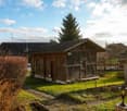Raised ground floor wooden house with brown roof, small garden, front door with porch