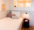 small bedroom with bed, pillows, nightstand, framed picture on wall, mirror on wall, drawers