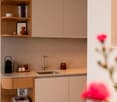 Modern kitchen with wooden cabinets, concrete countertop, sink with faucet, shelves with books and decorative items, flowers on the right side