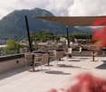 Outdoor seating area with tables, chairs, umbrella, plants, glass railing, mountain view