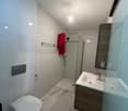 modern bathroom with white tiles, glass shower, white sink, wooden cabinet, white toilet