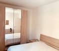 Bedroom with wooden bed, wooden wardrobe, mirror, nightstand, and small plant