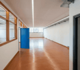 Empty room, brown floor, white walls, blue door, windows, ceiling lights
